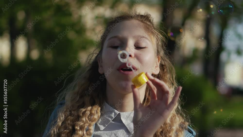 Young beautiful girl with luxurious curly hair launches soap bubbles in the park. Blonde having fun, smiling and posing for the camera. Young beautiful girl with luxurious curly hair launches soap bubbles in the park. Blonde having fun, smiling and posing for the camera.