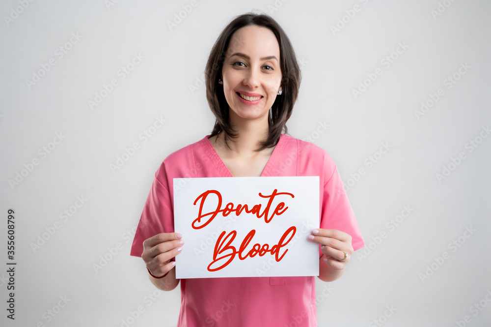 Smilieng woman medical professional nurse or doctor dressed with pink hospital clothes holding a paper whit message donate blood
