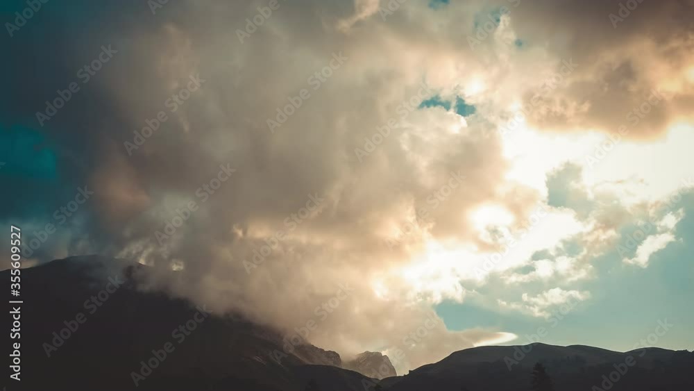 Wonderful landscape shot of huge clouds of a pinkish tint lying over the large Caucasus mountains covered with forests and grass, Adygea, Russia. Panoramic view of time laps of mountains and clouds. Wonderful landscape shot of huge clouds of a pinkish tint lying over the large Caucasus mountains covered with forests and grass, Adygea, Russia. Panoramic view of time laps of mountains and clouds.