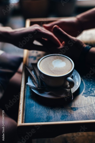 The couple in the cafe holds hands gently. A cup of coffee.