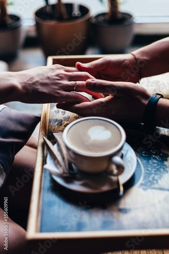 The couple in the cafe holds hands gently. A cup of coffee.