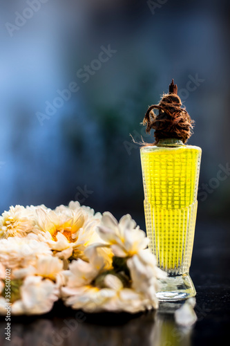 Scent or perfume of common daisy or English daisy in a glass bottle along with some daisy flowers on a black wooden board, with blurred background and selective focus. photo