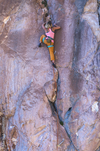 A strong woman climbs a beautiful orange rock.