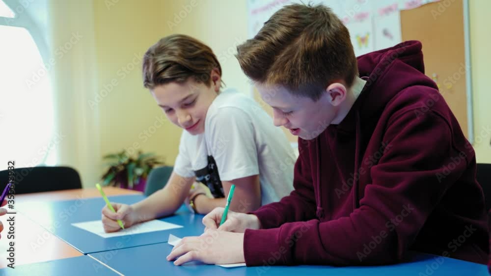 Students studying at school. Teenage boys sitting at the table and writing tasks in the modern classroom. Educational process. Students studying at school. Teenage boys sitting at the table and writing tasks in the modern classroom. Educational process.