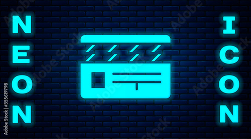 Glowing neon Movie clapper icon isolated on brick wall background. Film clapper board. Clapperboard sign. Cinema production or media industry. Vector Illustration.