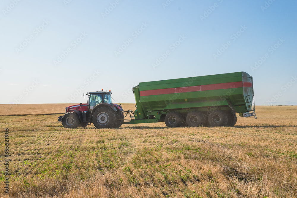 Grain harvest concept. Agricultural tractor with loader in mowed field on sunny day Grain harvest concept. Agricultural tractor with loader in mowed field on sunny day