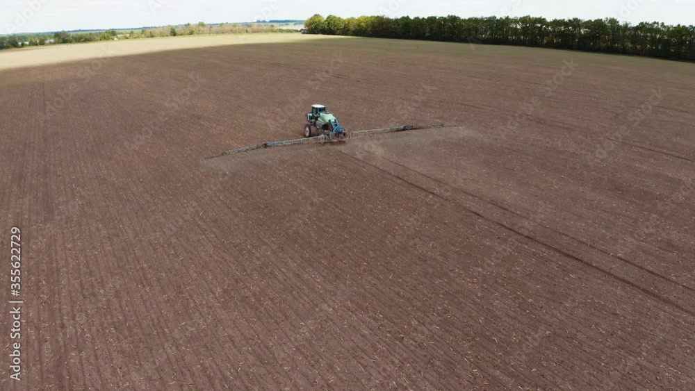 Agricultural field in spring. Tractor with special equipment spraying field. Flying over the field with machinery sprinkling chemicals during seasonal works. Aerial view. Agricultural field in spring. Tractor with special equipment spraying field. Flying over the field with machinery sprinkling chemicals during seasonal works. Aerial view.