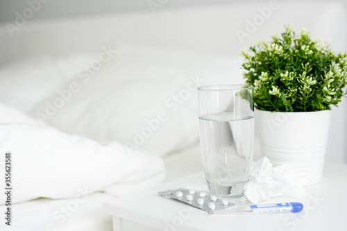 health care and illness concept - glass of water, pills and thermometer on bedside table