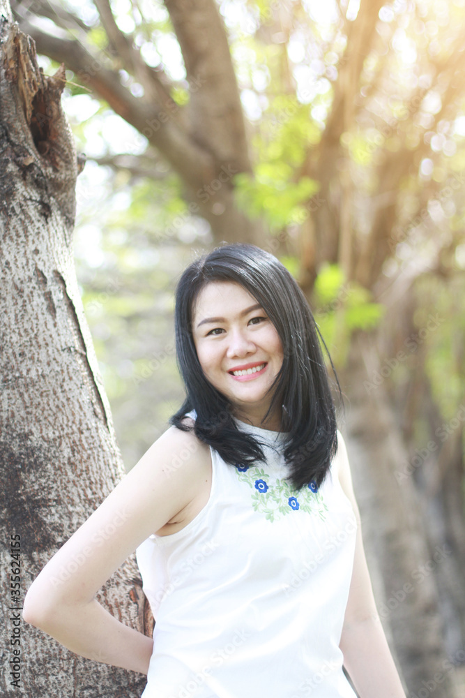 Beautiful asian woman in white dress relax and smiling in natural park. Thai girl or Chinese Girl enjoy on holiday with sunlight in garden Beautiful asian woman in white dress relax and smiling in natural park. Thai girl or Chinese Girl enjoy on holiday with sunlight in garden