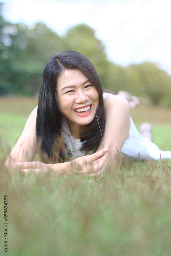 Beautiful asian woman in white dress relax and smiling on green field in natural park. Thai girl or Chinese Girl enjoy on holiday with sunlight in garden Beautiful asian woman in white dress relax and smiling on green field in natural park. Thai girl or Chinese Girl enjoy on holiday with sunlight in garden