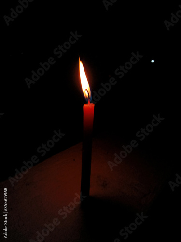 One tall lit candle on a dark background