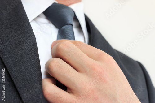 Close up of businessman with grey suit straightens his tie. Young caucasian elegant man's hand on gray necktie on isolated white background.