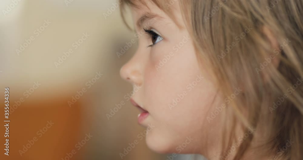 Adorable little girl in the sunlit living room watching tv and eating cereals