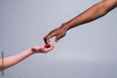 White caucasian female hand and black African American male hand holding fingers together in world unity and racial love and understanding in tolerance and races diversity. 