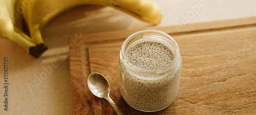 Dessert bowl of tasty chia seed pudding and banana on wooden table on white background. Banner for website