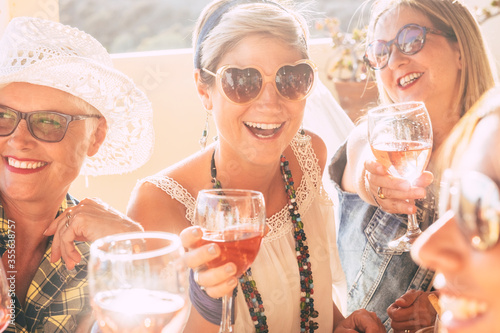 Cheerful group of happy women friends different ages adult and senior have fun together laughing and smiling and drinking wine during friendship celebration - people and social life concept