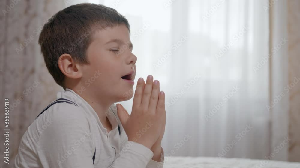 religion, prayer male child trust in God with hope in his heart and with folded together arms standing on wheels near bedstead in apartment, close-up religion, prayer male child trust in God with hope in his heart and with folded together arms standing on wheels near bedstead in apartment, close-up