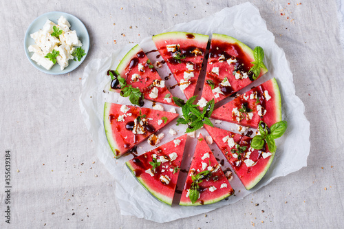 Watermelon pizza with feta cheese and herbs on a table