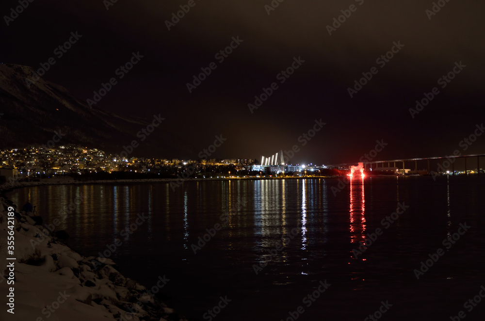 Beautiful firework on night sky in tromsoe city with bridge, cathedral and colorful reflection on the cold fjord water surface on new years eve