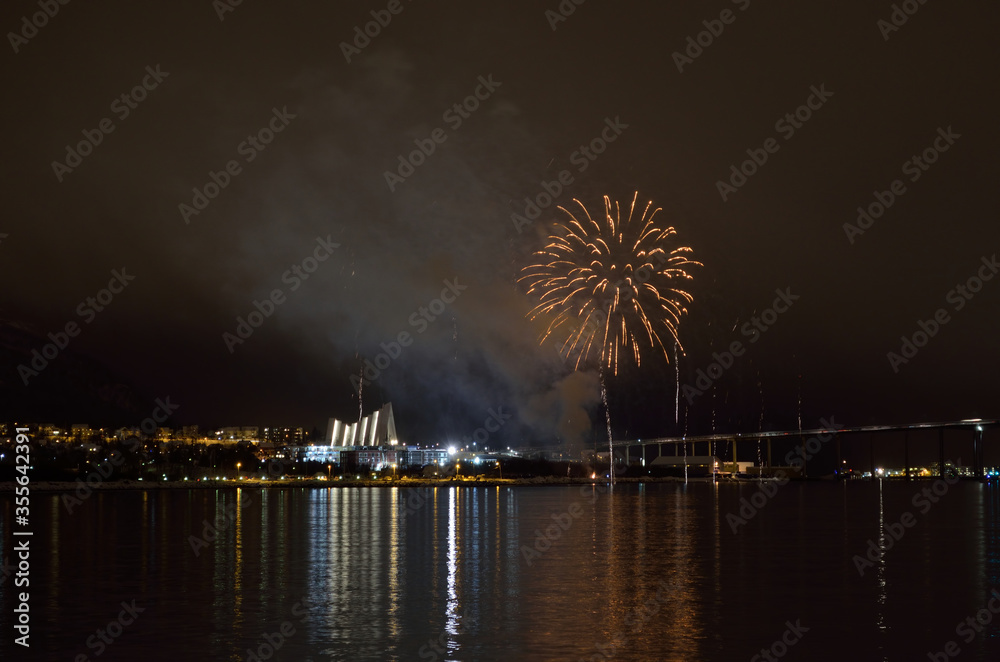 Beautiful firework on night sky in tromsoe city with bridge, cathedral and colorful reflection on the cold fjord water surface on new years eve