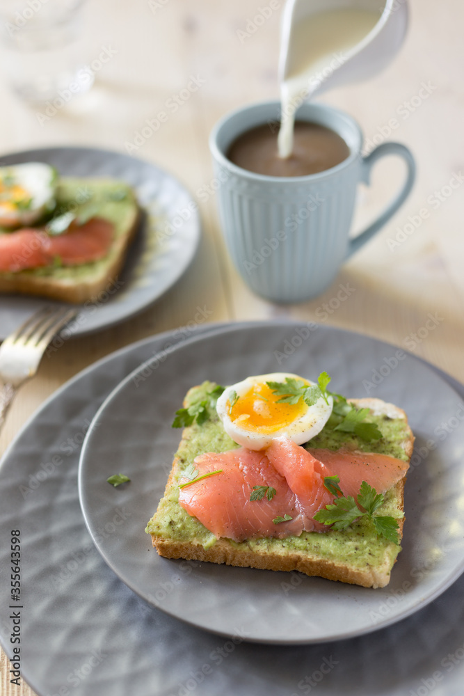 Sandwich with salmon, avocado, and egg on wood table.