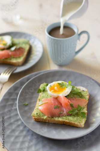 Sandwich with salmon, avocado, and egg on wood table.