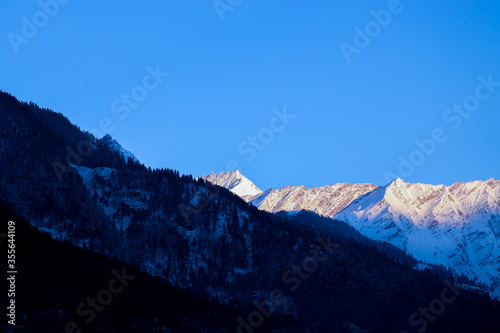 sunrise on the top of a snow-covered mountain. The mountain in the front is covered with pine trees. focus on infinity.