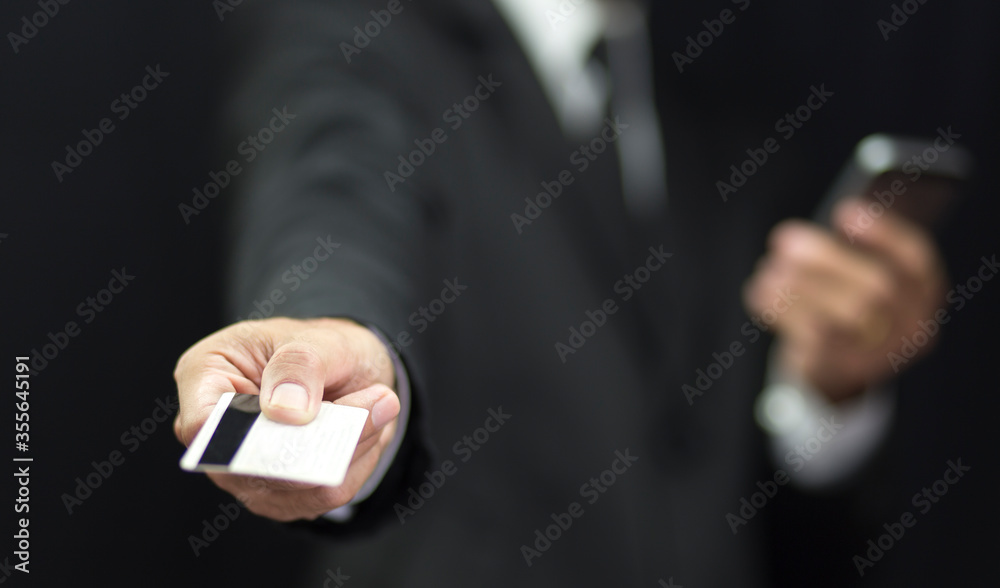 Fototapeta premium Businessman in black suit holding credit card and using smartphone background, Banking concept
