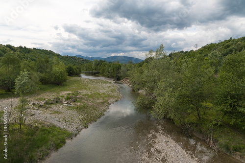 A Beautiful Quiet River Flowing near the Green Forest Towards the Mountains and the Dark Storm Clouds