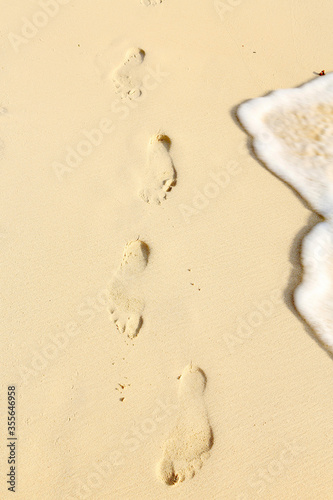 footprints next to gently lapping waves on a golden beach