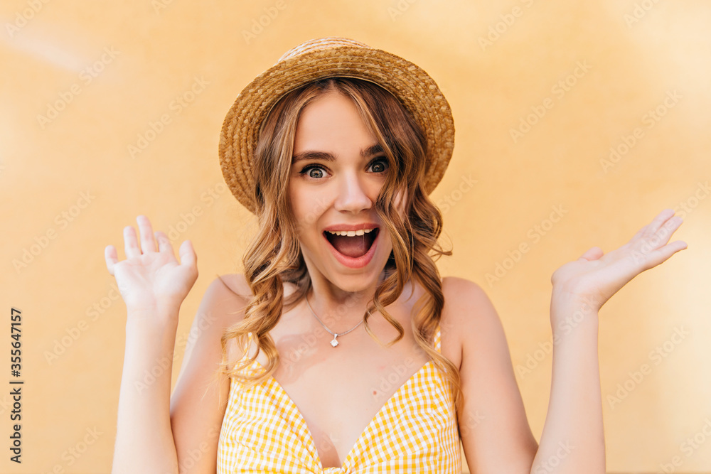 Surprised caucasian woman with wavy hairstyle posing in trendy hat. Portrait of debonair girl isolated on yellow background.