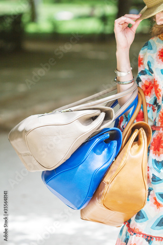 Front view of fashion girl with three leather handbags hanging from her arm. © Daniel