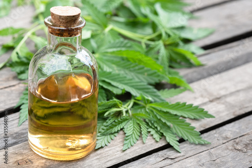 Cannabis CBD oil bottles and green plant leaves on dirty wooden table background.