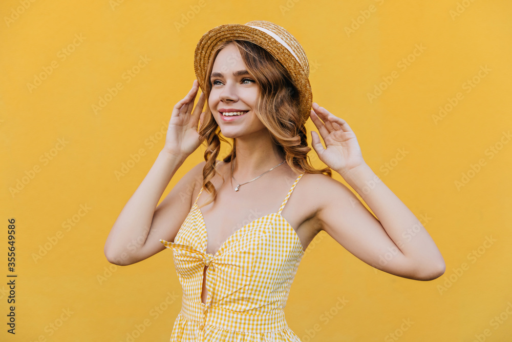 Blithesome white girl in straw hat dreamy looking away. Studio portrait of refined pretty lady wears stylish yellow dress.