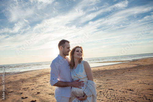 Love, wait for the baby. Portrait of a beautiful couple in white kissing on the background of the sunset sea.