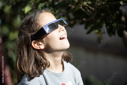 smiling girl watching an eclipse of the sun with eclipse glasses