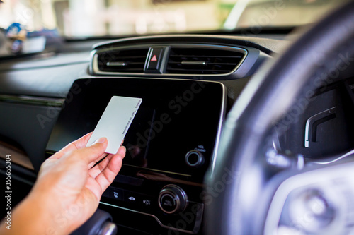 Selective focus to the driver's hand holds a smart card to read the information on the smart monitor screen at the console in the car. The concept of smart car.