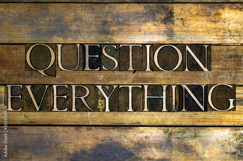Photo of real authentic typeset letters forming Question Everything text on vintage textured silver grunge copper and gold background