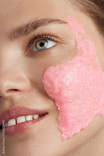 Face masks are the perfect treatment to hydrate skin, remove excess oils and improve the appearance of pores. Cropped shot of a smiling lady's face with pink grained mask on the skin. photo