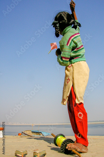 Varanasi, India. Back view of hindu girl playing with her kite in the Ghats of Varanasi with river Ganges in the background. 