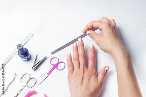Female hands hold a nail file  next to lay down devices for nail care. The girl does a manicure. on white background. View from above