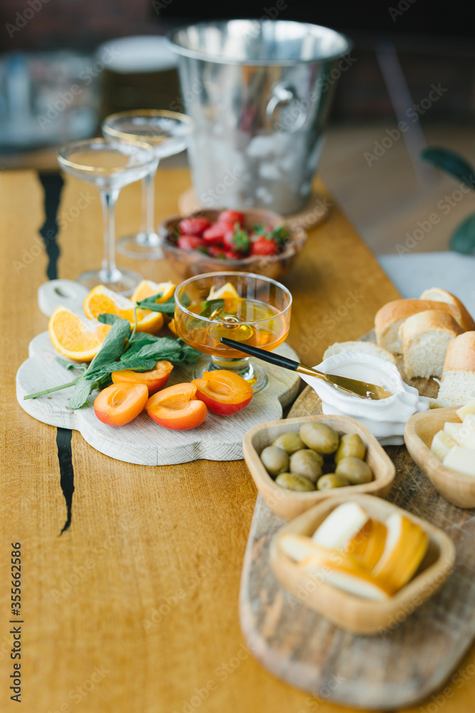 Snacks for an aperitif. Strawberries, cheese, olives, peach, oranges, bread, honey, champagne glasses and champagne in an ice bucket. Snacks for an aperitif. Strawberries, cheese, olives, peach, oranges, bread, honey, champagne glasses and champagne in an ice bucket.