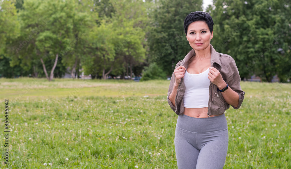 Young woman fitness trainer in stylish clothes stands on the football field against the background of summer greenery