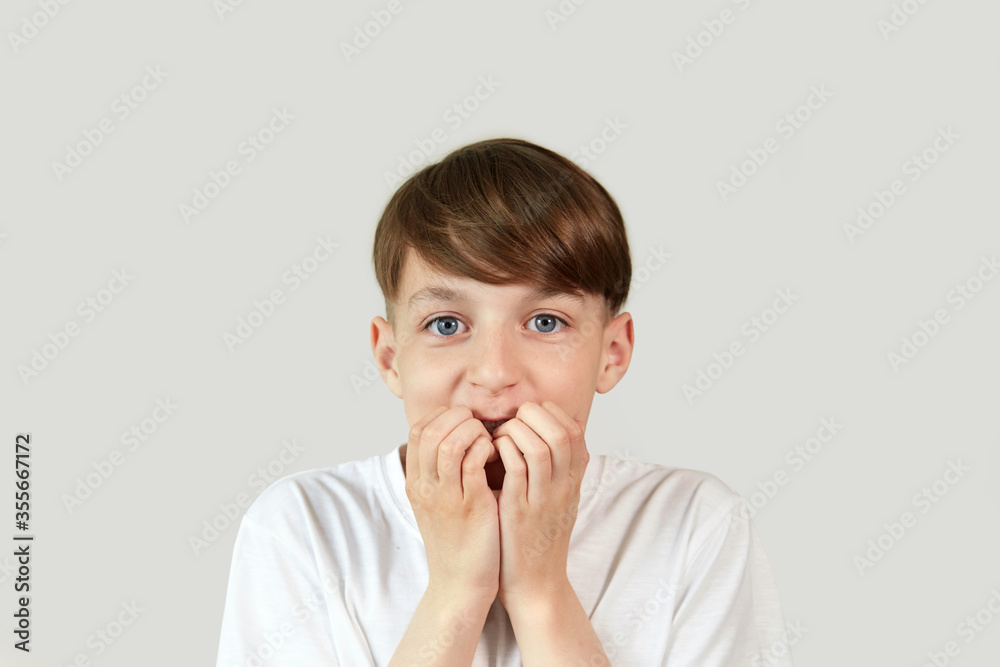 A boy with his eyes wide open looks scared at the camera. Hands at the mouth. A boy with his eyes wide open looks scared at the camera. Hands at the mouth.