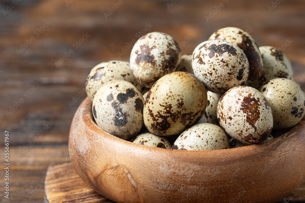 Fresh quail eggs in a wooden bowl on a brown wooden table. Raw quail eggs close-up on a culinary background. Concept of preparation for cooking Fresh quail eggs in a wooden bowl on a brown wooden table. Raw quail eggs close-up on a culinary background. Concept of preparation for cooking