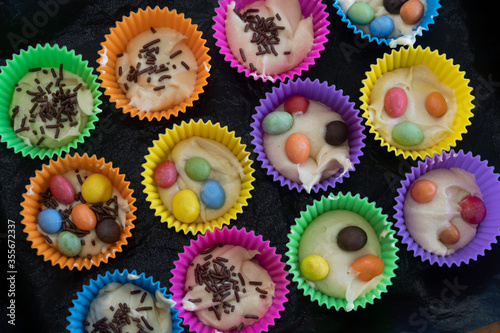 Obraz na płótnie Delicious pastry cooked at home. Homemade cupcakes in multi-colored silicone molds and with colored chocolates inside on a baking tray. w salonie