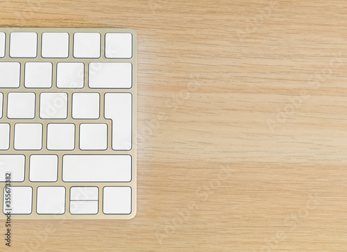 half an aluminium keyboard with blank white keys on a light wooden background