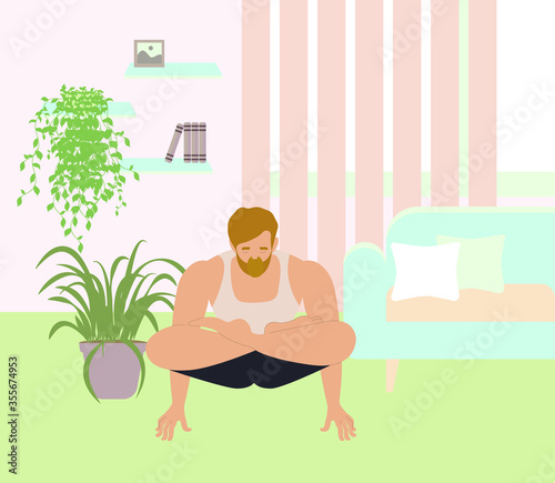 A young hipster practices yoga or fitness in his apartment. Concept: training, gymnastics, acrobatics, concentration, balance, health, interior, isolation, immunity, staying at home, coordination. 