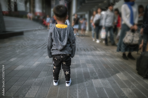 Small kid standing alone in big city while group of people walking in the street