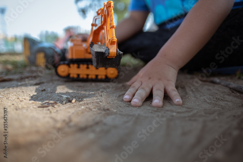 Little kid playing excavator toy on the sand ground